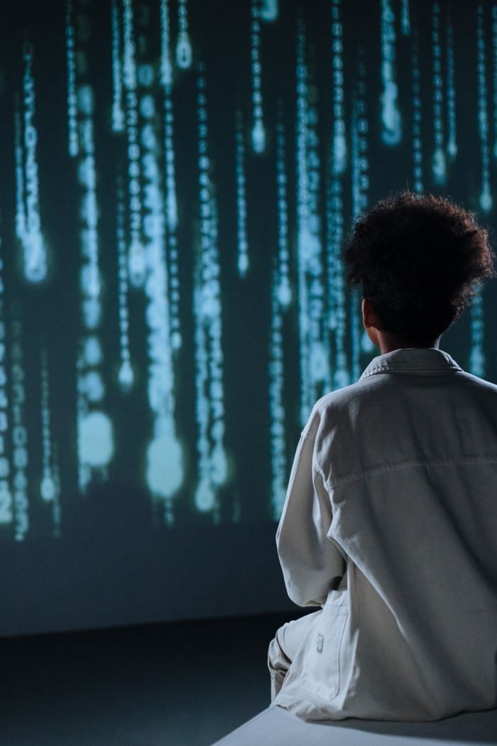 Teenager sitting in front of digital screen with abstract code projection.